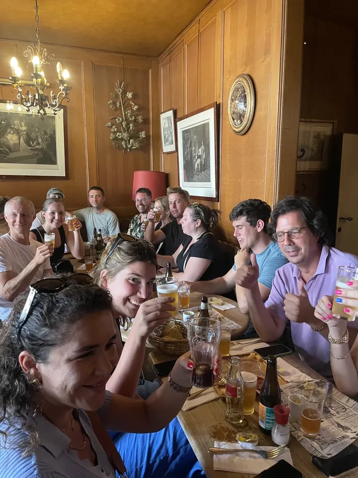A long table of people in a wood-panelled room, glasses raised in a toast, everyone talking at once.